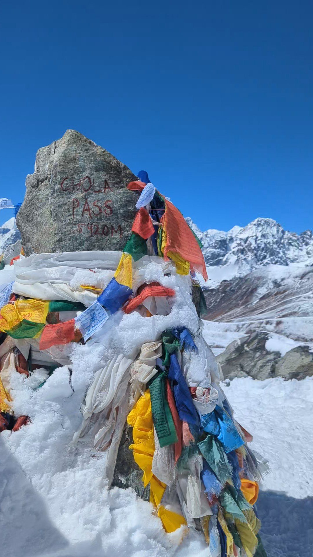 Cumulo di pietre segnato dalla scritta “Cho La Pass 5420 m”, avvolto da bandiere di preghiera colorate che sventolano nel vento himalayano.